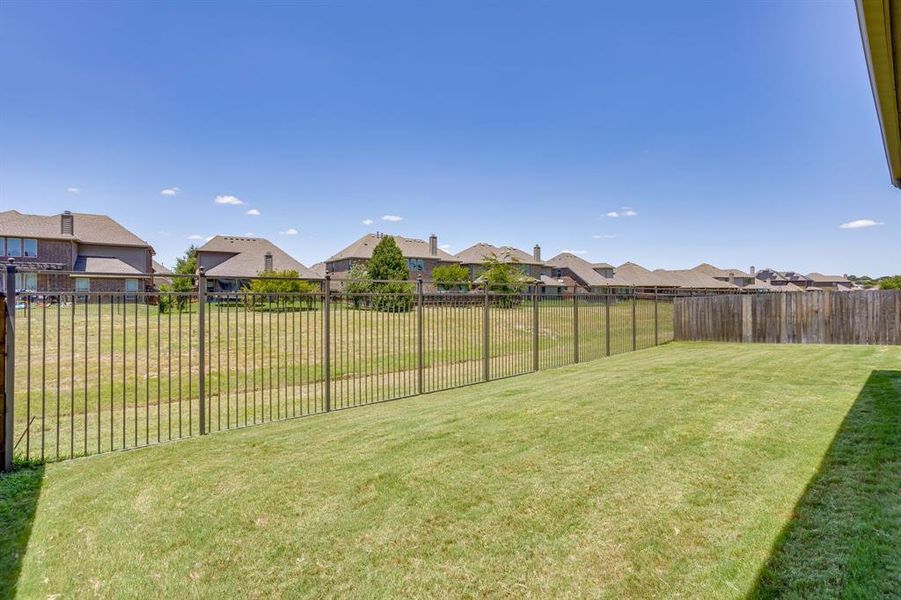 Expansive backyard featuring a manicured lawn, a combination of metal and wood fencing, and open sky