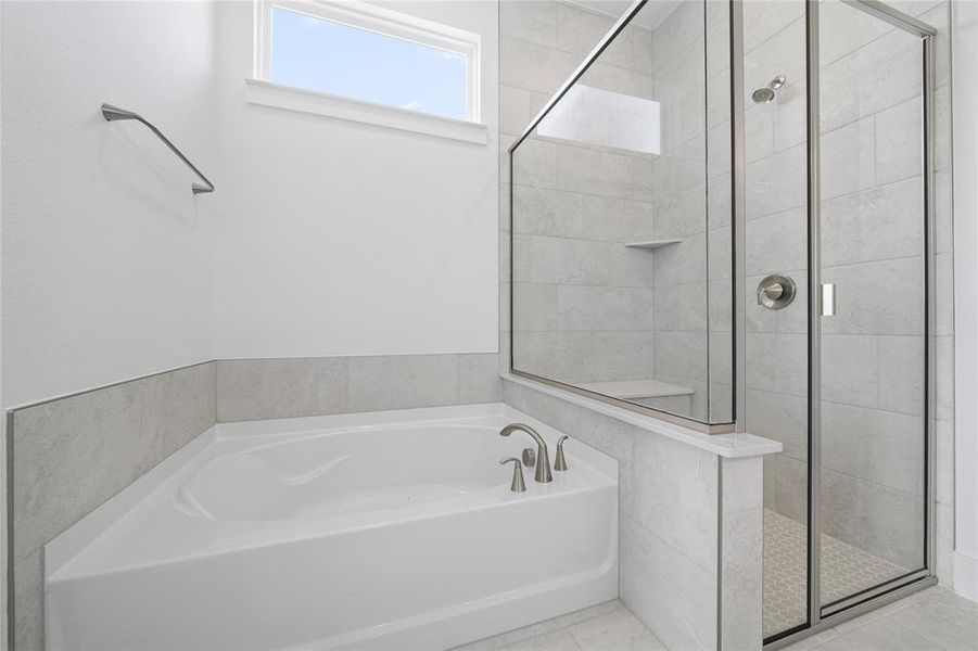 Corner soaking tub with deck-mounted brushed nickel fixtures, complemented by a glass-enclosed shower with a built-in bench and a tile-finished shower floor