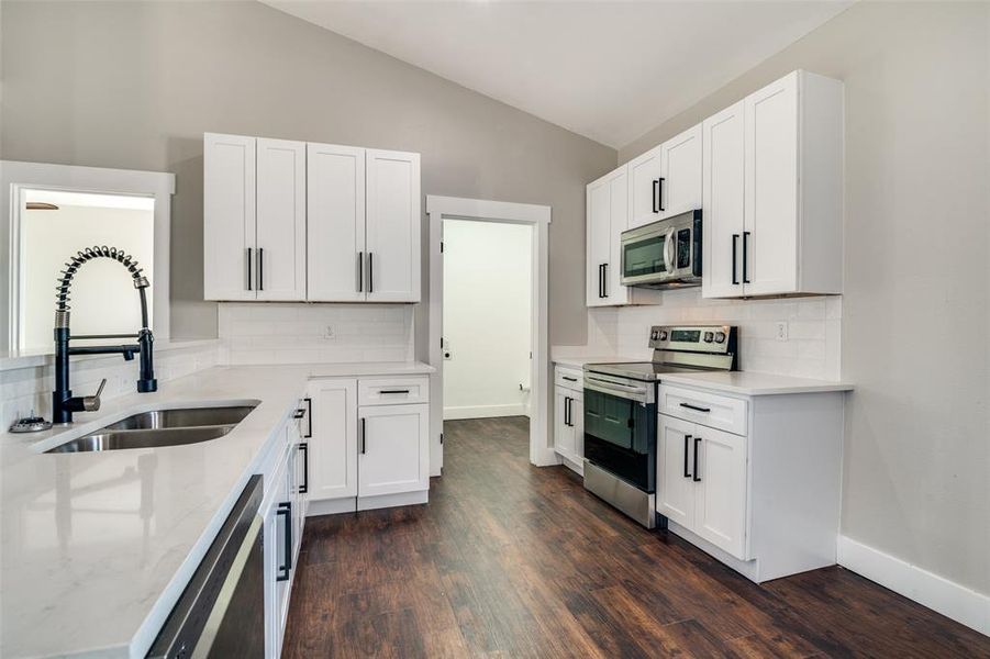 Kitchen with decorative backsplash, dark hardwood / wood-style flooring, stainless steel appliances, sink, and white cabinetry