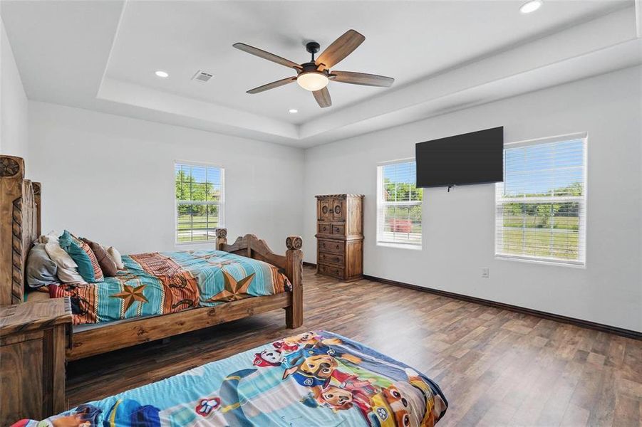 Bedroom with wood finished floors, multiple windows, a ceiling fan, a raised ceiling, and recessed lighting Bedroom with wood finished floors, multiple windows, a ceiling fan, a raised ceiling, and recessed lighting