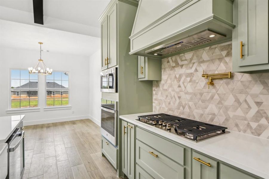 Kitchen featuring backsplash, green cabinetry, custom exhaust hood, and stainless steel appliances Kitchen featuring backsplash, green cabinetry, custom exhaust hood, and stainless steel appliances