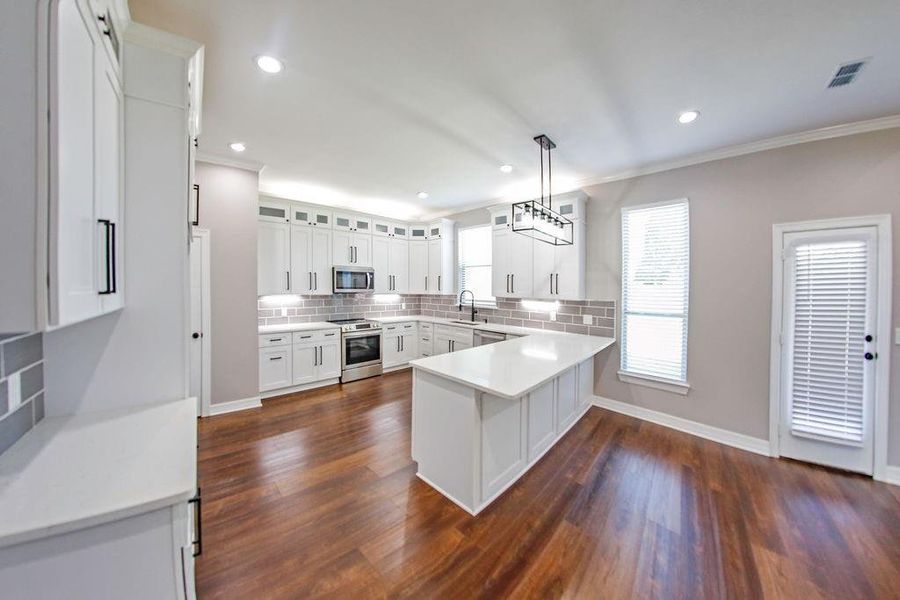 Kitchen featuring decorative backsplash, pendant lighting, white cabinetry, stainless steel appliances, and a peninsula Kitchen featuring decorative backsplash, pendant lighting, white cabinetry, stainless steel appliances, and a peninsula