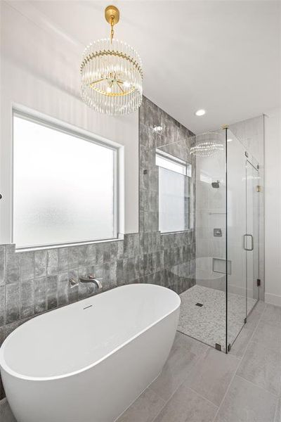 Freestanding soaking tub with a wall-mounted faucet, complemented by a spacious glass-enclosed shower with mosaic tile flooring