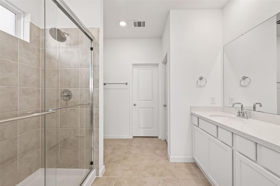 Primary Bathroom features elevated ceilings with recessed lighting and a calming neutral palette, creating a bright and serene atmosphere. It is appointed with double vanities offering generous counter space and storage, along with a sleek glass-enclosed shower. Thoughtfully designed, this space provides a refined setting for both comfort and everyday functionality.