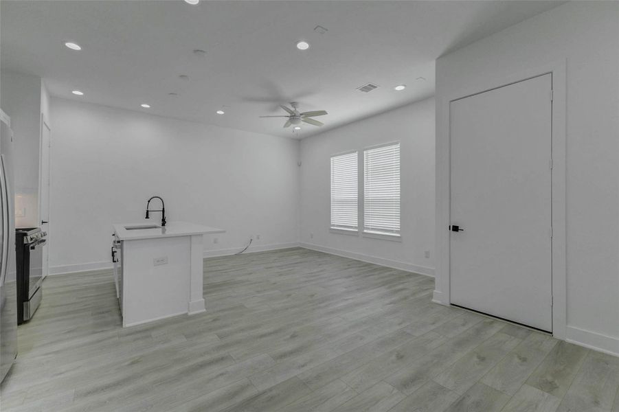 The second-floor living space opens beneath high ceilings with light wood-look flooring, recessed lighting, a ceiling fan, and a direct connection to the kitchen and dining area. The open arrangement encourages conversation and effortless movement between everyday activities.