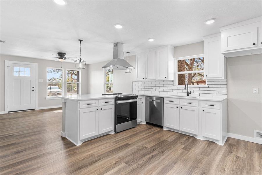 Kitchen with white cabinetry, appliances with stainless steel finishes, backsplash, island exhaust hood, and recessed lighting