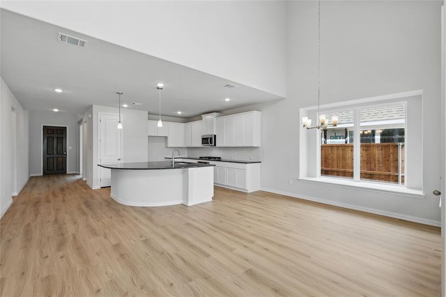 Kitchen with stainless steel microwave, dark countertops, visible vents, baseboards, and light wood-type flooring Kitchen with stainless steel microwave, dark countertops, visible vents, baseboards, and light wood-type flooring