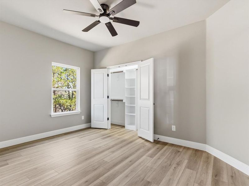 Unfurnished bedroom with a walk in closet, light wood finished floors, and ceiling fan Unfurnished bedroom with a walk in closet, light wood finished floors, and ceiling fan