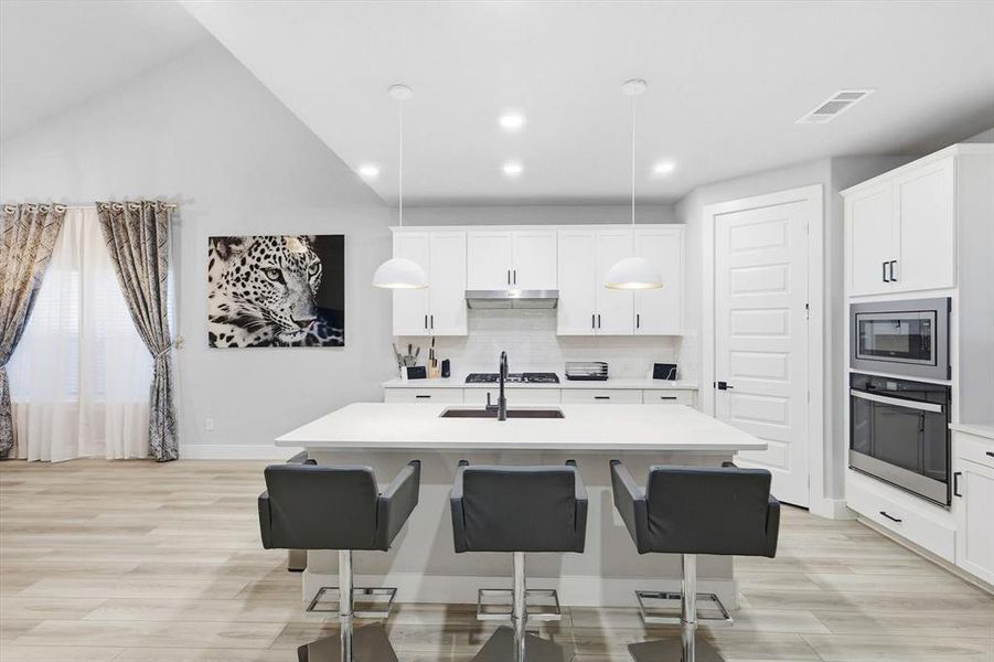 Kitchen featuring a kitchen breakfast bar, appliances with stainless steel finishes, decorative backsplash, white cabinets, and decorative light fixtures