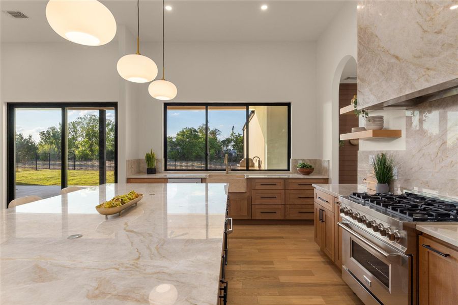 Kitchen featuring high end stainless steel range, hanging light fixtures, light stone counters, decorative backsplash, and wood finish cabinetry