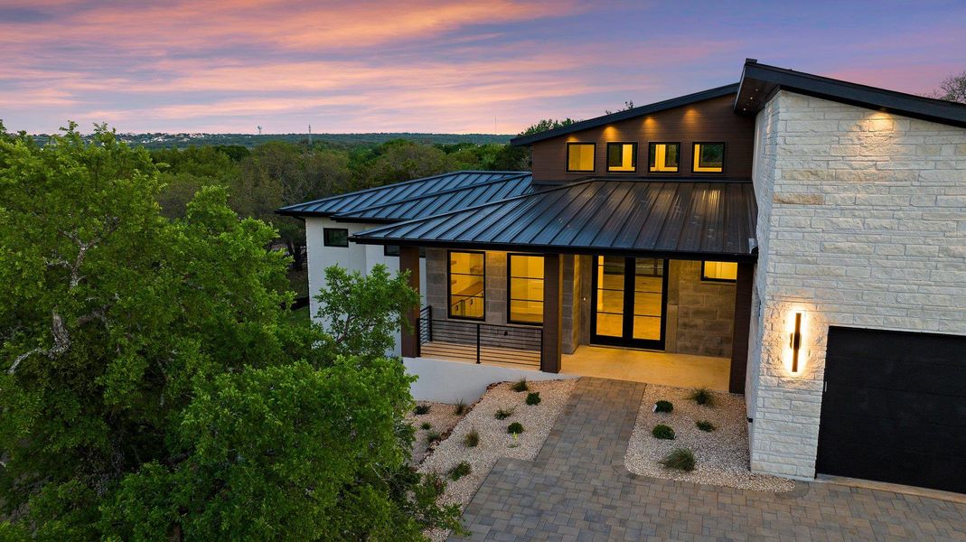 A striking contemporary residence with a modern metal roof and stone facade under a vibrant sunset sky.