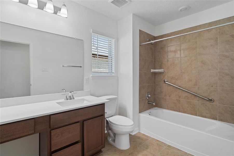 Secondary bathroom features light countertops and stained cabinets, neutral paint, shower/tub combo with tile surround, large mirror, tile floors, sleek fixtures and modern finishes, plenty of space to accommodate any visiting family or guests.