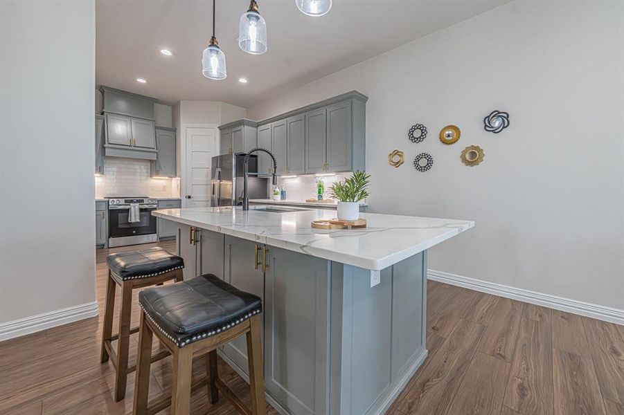 Kitchen featuring gray cabinets, tasteful backsplash, a breakfast bar area, hanging light fixtures, and a kitchen island with sink Kitchen featuring gray cabinets, tasteful backsplash, a breakfast bar area, hanging light fixtures, and a kitchen island with sink