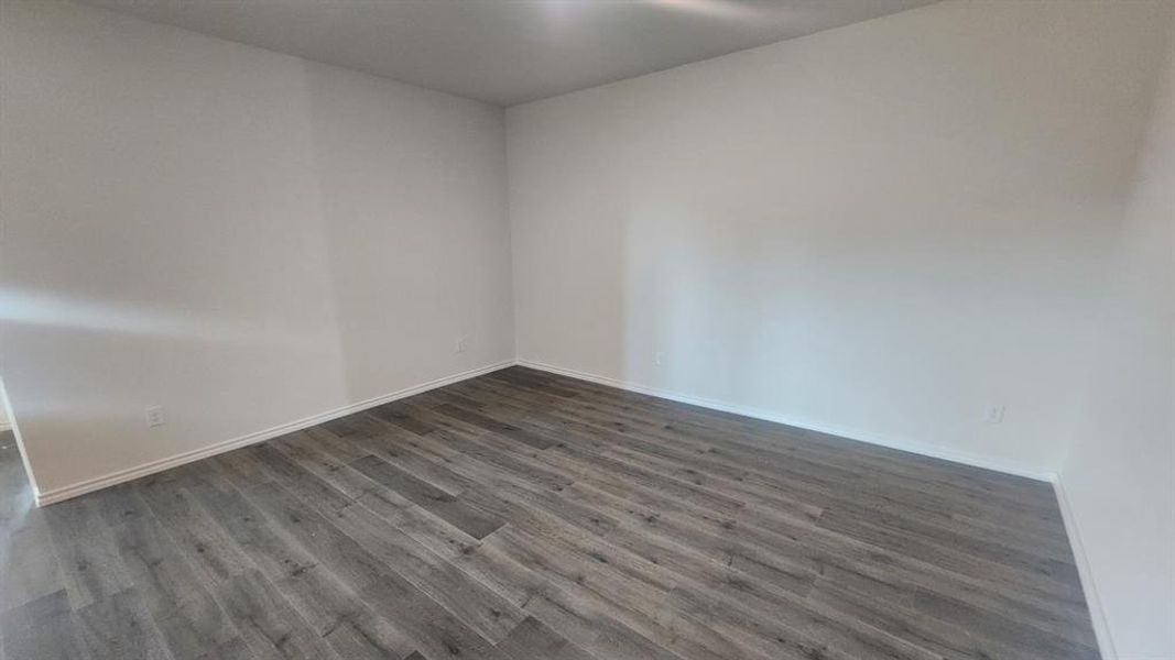 Spacious interior room featuring wood-finish flooring, white baseboards, and neutral wall tones