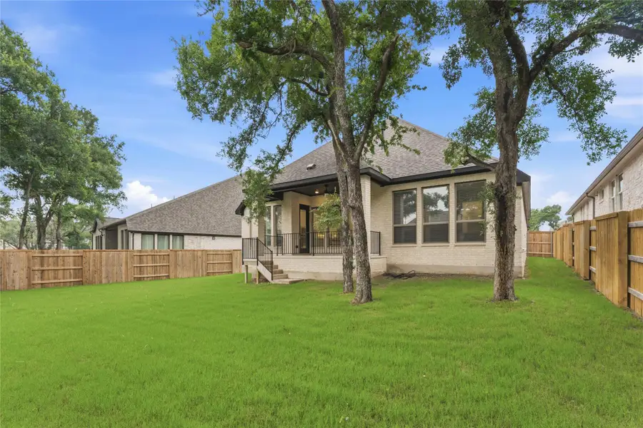 Expansive backyard featuring a lush lawn, two mature trees, and a full privacy fence