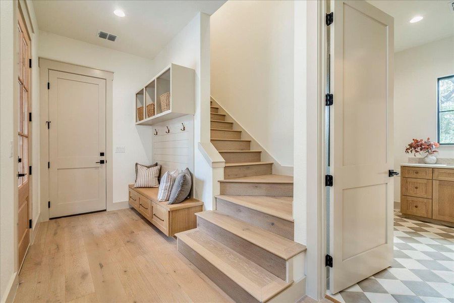A welcoming entry offers a built-in bench and practical coat hooks, with light hardwood stairs leading upward.