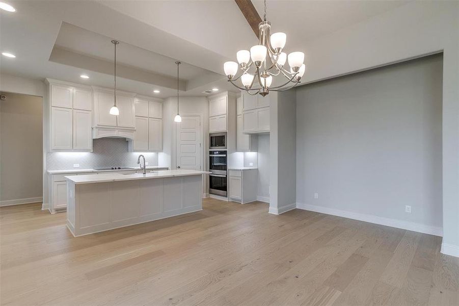 Kitchen with light hardwood / wood-style flooring, pendant lighting, and a tray ceiling