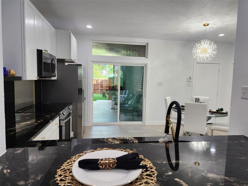 Kitchen with stainless steel appliances, pendant lighting, dark stone countertops, and white cabinetry