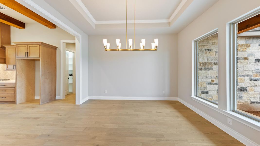 Unfurnished dining area featuring light wood-style flooring, a raised ceiling, a chandelier, and ornamental molding