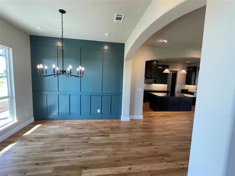 Dining area featuring a decorative teal accent wall with panel molding, a black ten-light chandelier, and wood-finish flooring