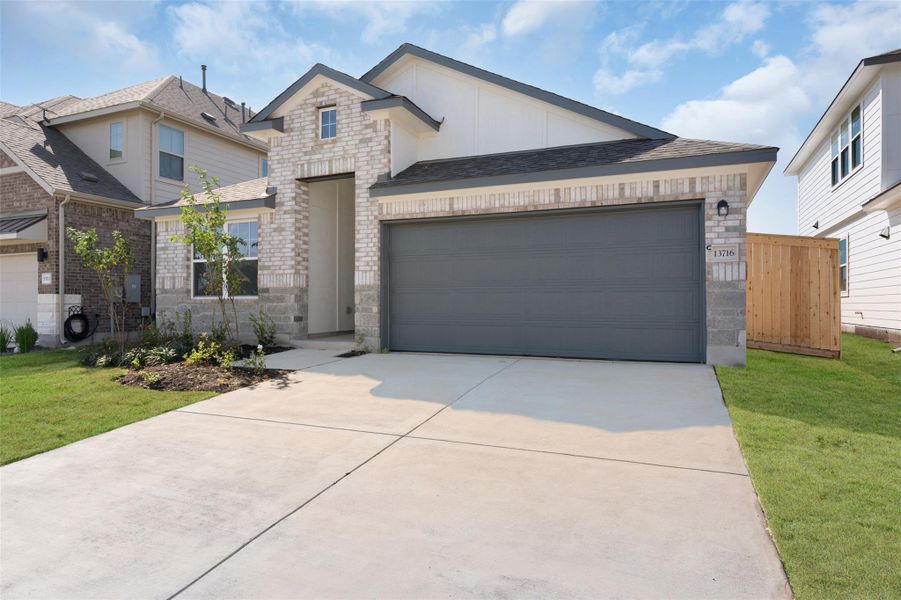 View of front facade featuring a garage, brick siding, concrete driveway, board and batten siding, and a front yard