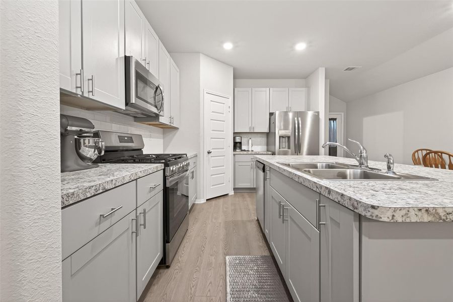 This modern kitchen features sleek stainless steel appliances, white cabinetry, and granite countertops. It includes a spacious island with a double sink and ample storage. The layout is open and inviting, perfect for cooking and entertaining.