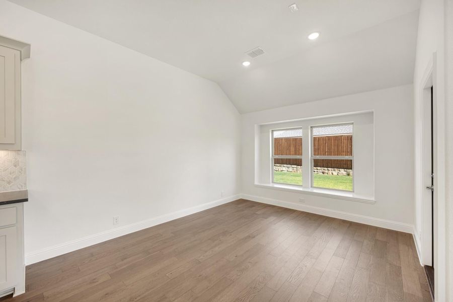 Empty dining or living area with vaulted ceiling, hardwood floors, and a double window overlooking backyard