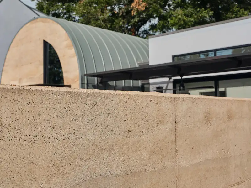 Crowning the structure are barrel-vaulted roofs clad in soft green metal, which curve downward to become walls—emphasizing the fluidity of the architecture and highlighting the homes’ sculptural forms.