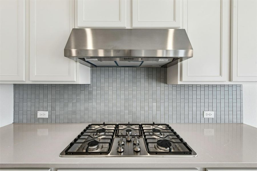 Kitchen with exhaust hood, stainless steel gas stovetop, light stone countertops, and white cabinetry