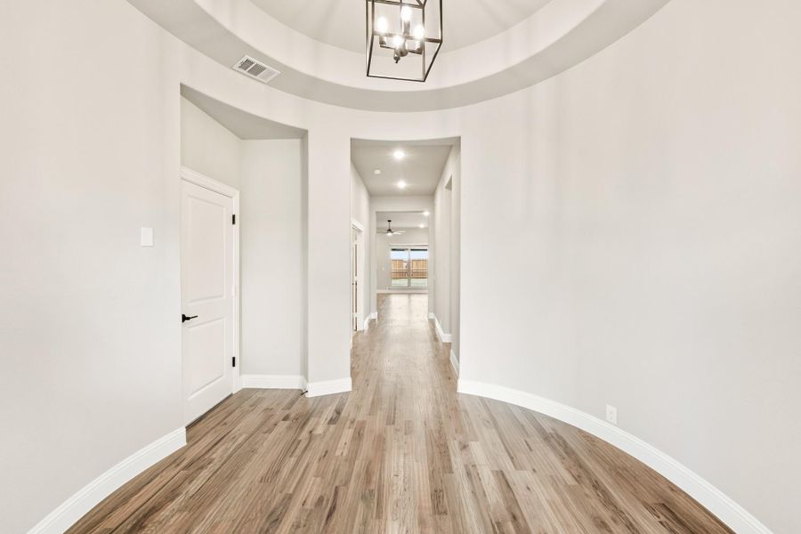 Circular foyer with round tray ceiling, pendant chandelier, wood floors, and hallway leading to main living area Circular foyer with round tray ceiling, pendant chandelier, wood floors, and hallway leading to main living area