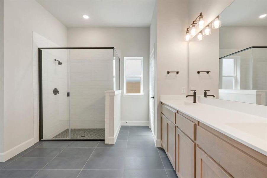 Spacious bathroom featuring a glass-enclosed shower with subway tile, a double vanity with light wood-finish cabinetry, white countertops, and matte black fixtures