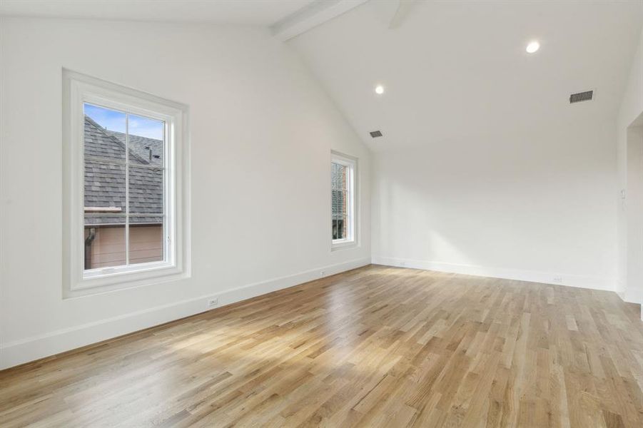 Primary bedroom featuring high vaulted ceiling, a wealth of natural light, light hardwood / wood-style floors, and beamed ceiling