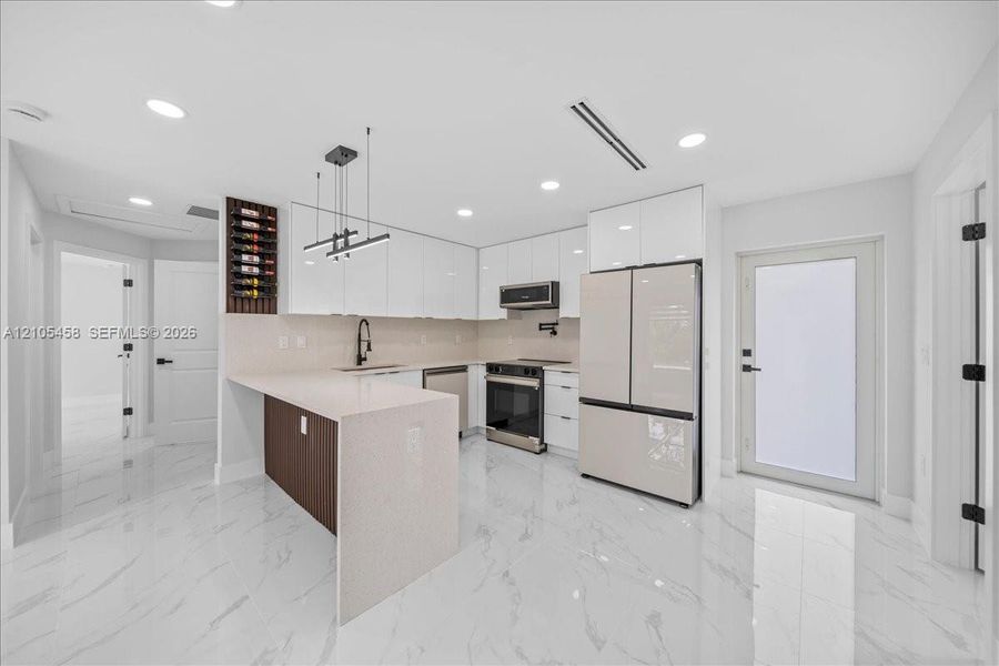 Contemporary kitchen featuring white flat-panel cabinetry, a built-in wine rack, light-toned countertops, and stainless steel appliances Contemporary kitchen featuring white flat-panel cabinetry, a built-in wine rack, light-toned countertops, and stainless steel appliances