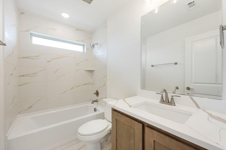 Bathroom with marble-look tile tub surround, wood vanity with white quartz countertop, and large mirror Bathroom with marble-look tile tub surround, wood vanity with white quartz countertop, and large mirror