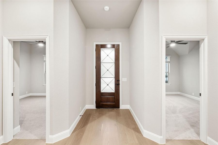 Entryway with dark wood front door with glass panels, light hardwood floors, and openings to two carpeted rooms.