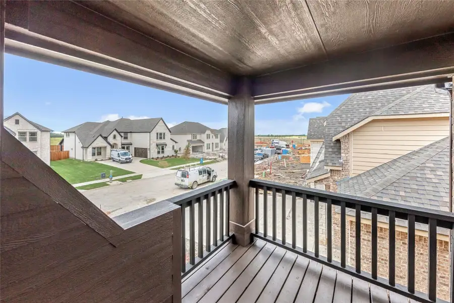 Covered second-floor balcony with dark wood railing overlooking a new home subdivision under construction