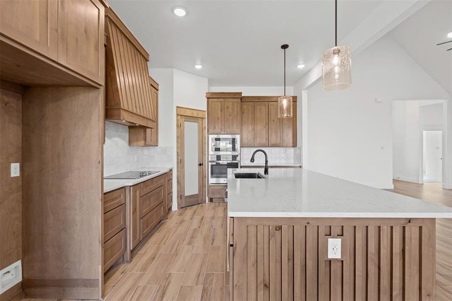 Kitchen with brown cabinets, light wood finished floors, backsplash, decorative light fixtures, and appliances with stainless steel finishes