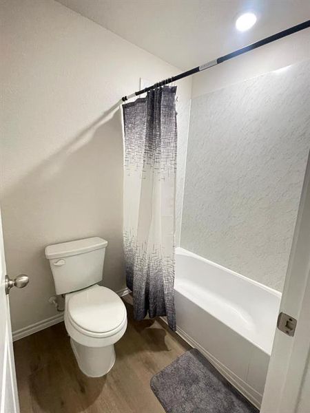 Bathroom featuring wood-type flooring, toilet, and shower / bath combo with shower curtain