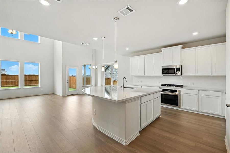 Kitchen with decorative backsplash, decorative light fixtures, a kitchen island with sink, white cabinets, and recessed lighting