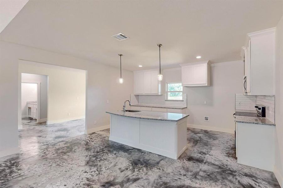 Kitchen featuring pendant lighting, a kitchen island with sink, sink, tasteful backsplash, and white cabinetry