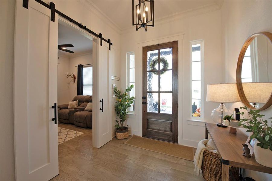 Entryway featuring a barn door, light wood-type flooring, crown molding, and a chandelier