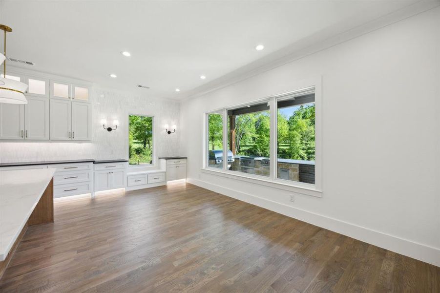 Kitchen with recessed lighting, glass insert cabinets, white cabinetry, wood finished floors, and hanging light fixtures Kitchen with recessed lighting, glass insert cabinets, white cabinetry, wood finished floors, and hanging light fixtures