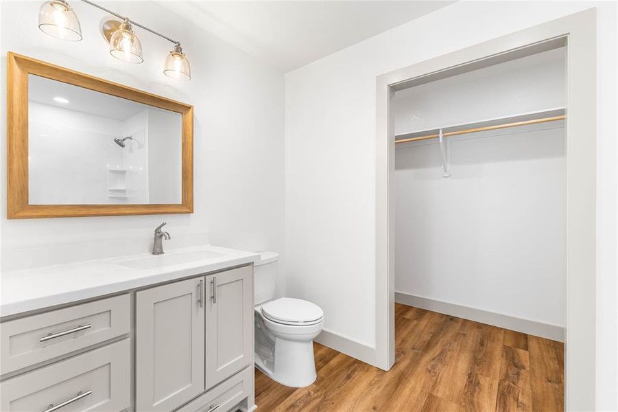 Full bathroom with toilet, vanity, wood finished floors, a spacious closet, and a shower Full bathroom with toilet, vanity, wood finished floors, a spacious closet, and a shower