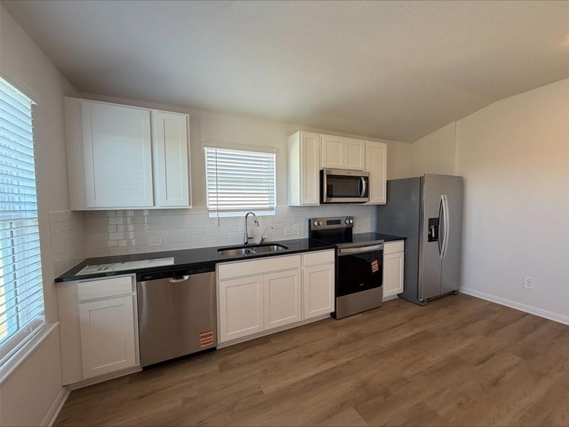 Kitchen featuring stainless steel appliances, white cabinets, tasteful backsplash, lofted ceiling, and dark wood-type flooring