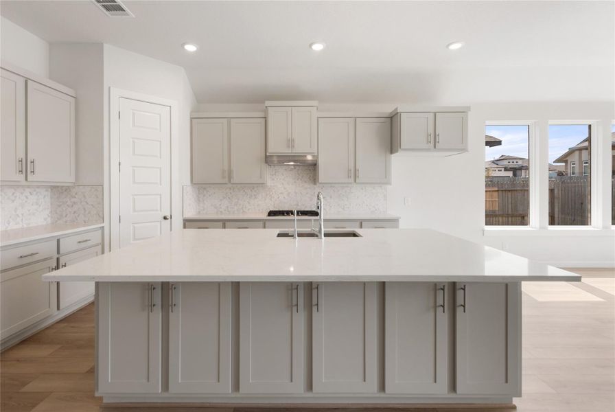 Kitchen featuring light stone counters, backsplash, light wood-style floors, recessed lighting, and a center island with sink