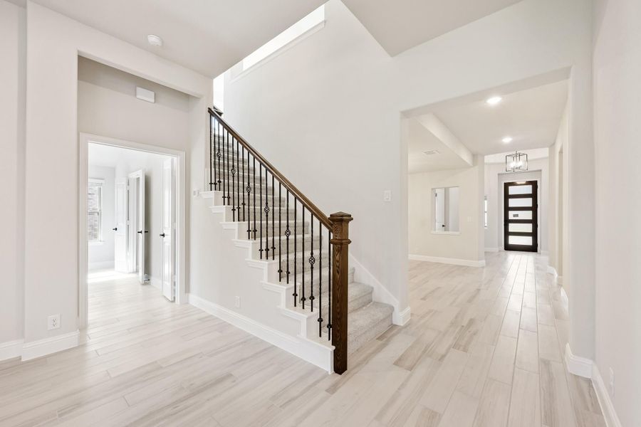 Bright home entryway with staircase featuring wood and iron railing, light hardwood floors, and front door view. Bright home entryway with staircase featuring wood and iron railing, light hardwood floors, and front door view.
