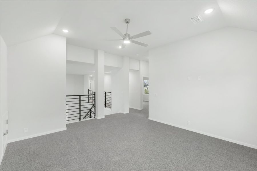 Open upstairs living area with gray carpet, ceiling fan, and modern black metal stair railing