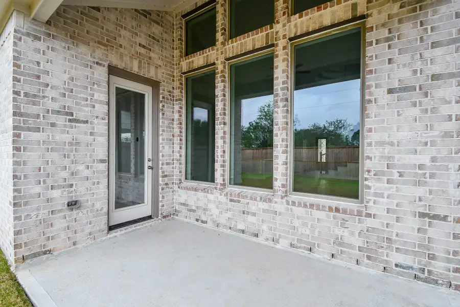 A cozy covered patio with brick accents and large windows, perfect for outdoor relaxation.
