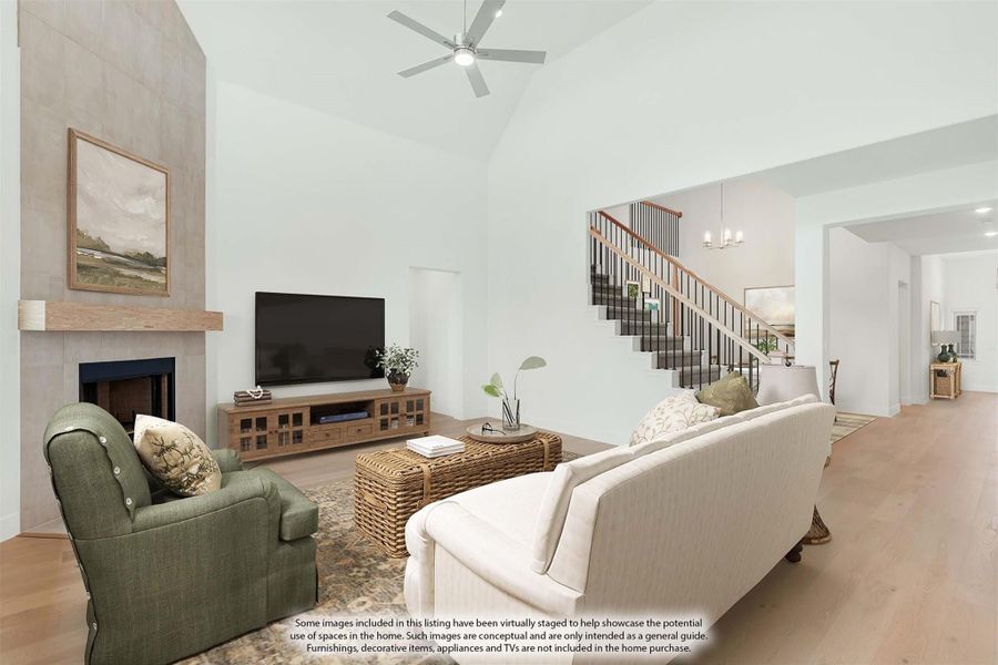 Living room with vaulted ceiling, tile fireplace, ceiling fan, and staircase visible in background