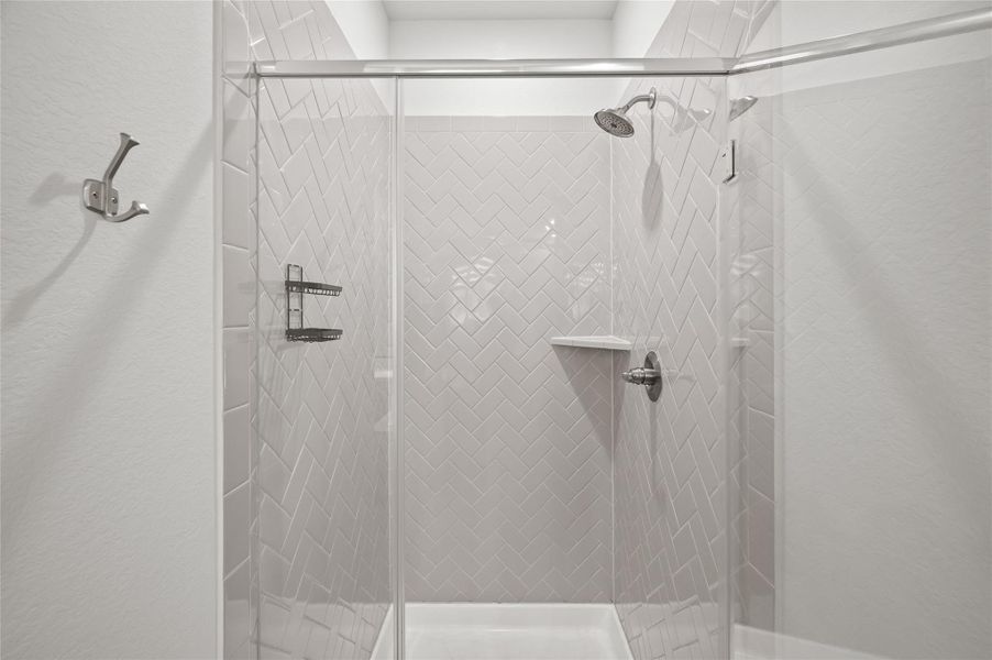 Stunning primary shower with upgraded herringbone tile and a frameless glass enclosure.